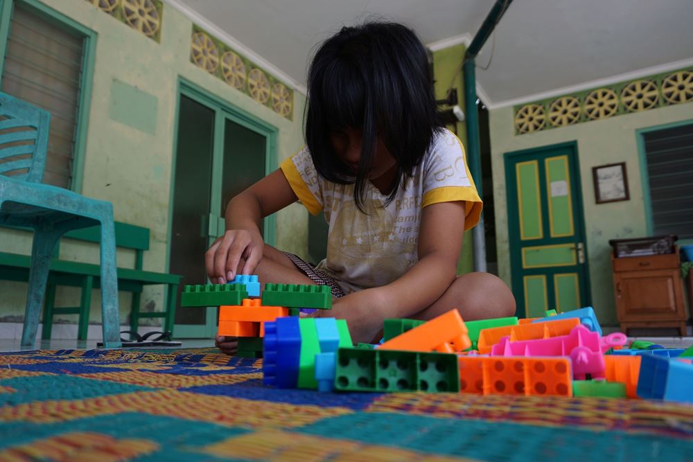 Ein Mädchen aus Indonesien sitzt auf dem Boden und spielt mit buntem Spielzeug. (Quelle: Christiane Dase)