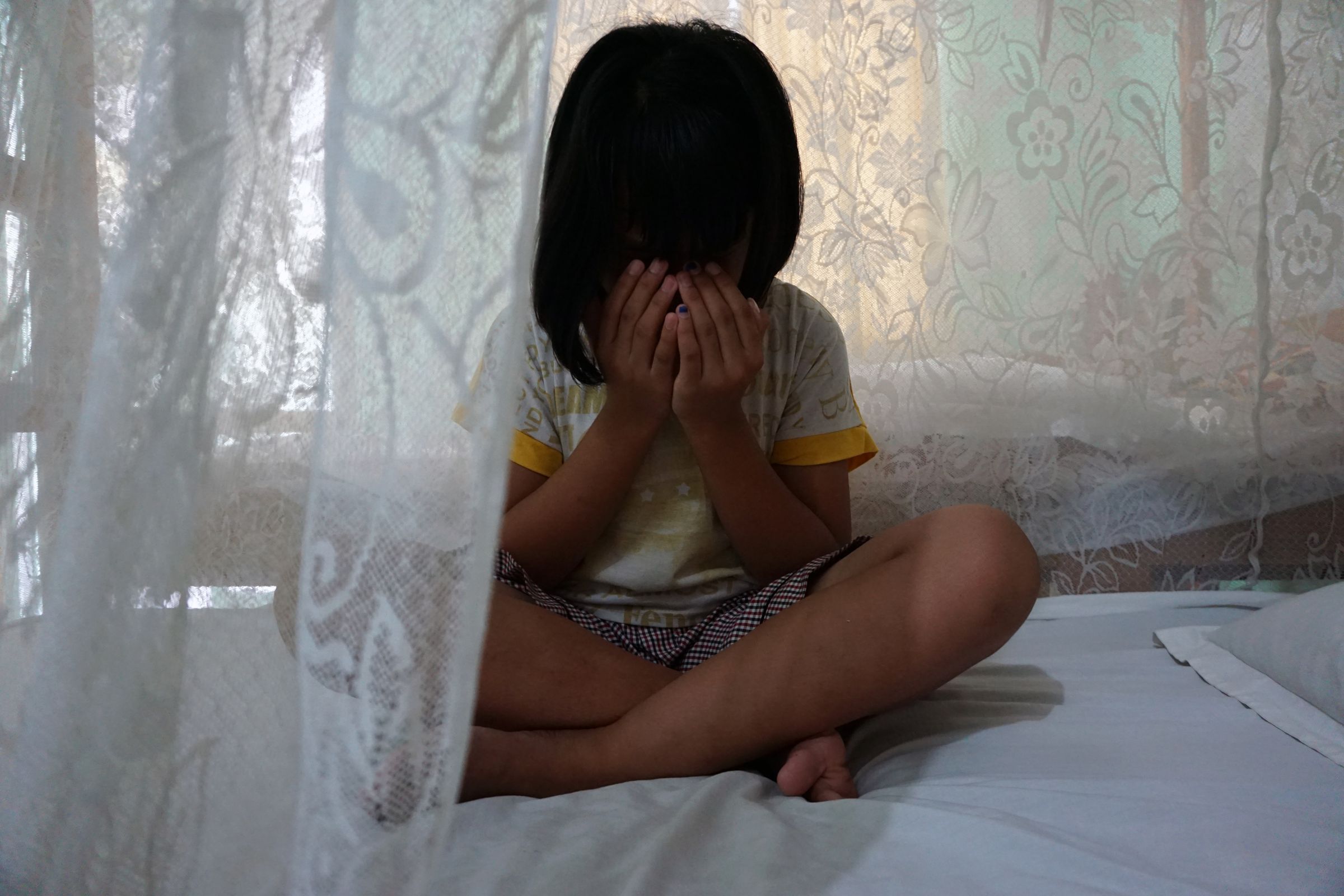 Ein Mädchen aus Indonesien sitzt auf einem Bett und vergräbt das Gesicht in ihren Händen. (Quelle: Christiane Dase)