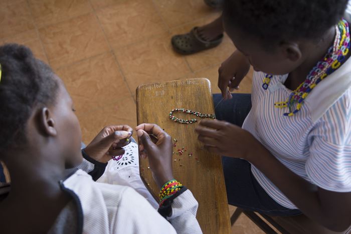 Zwei Mädchen knüpfen eine Perlenkette in einem Schutzhaus in Kenia. (Quelle: Christian Nusch)