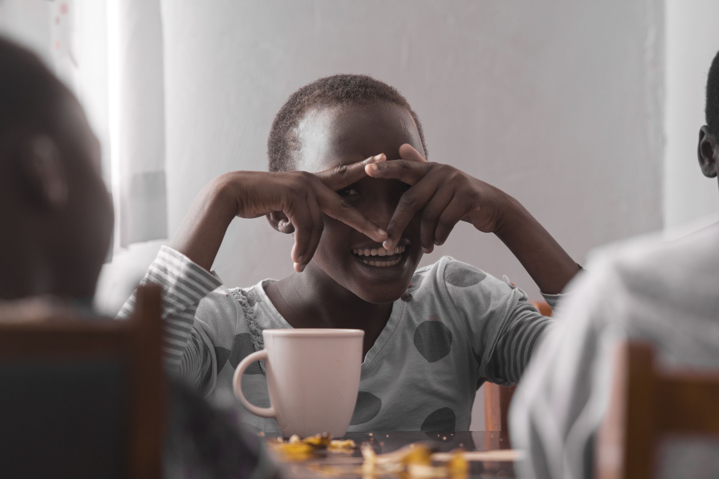 Rosa, ein Mädchen im Schutzhaus in Kenia, sitzt am Tisch, schaut durch ihre Hände und lacht. (Quelle: Christian Nusch)