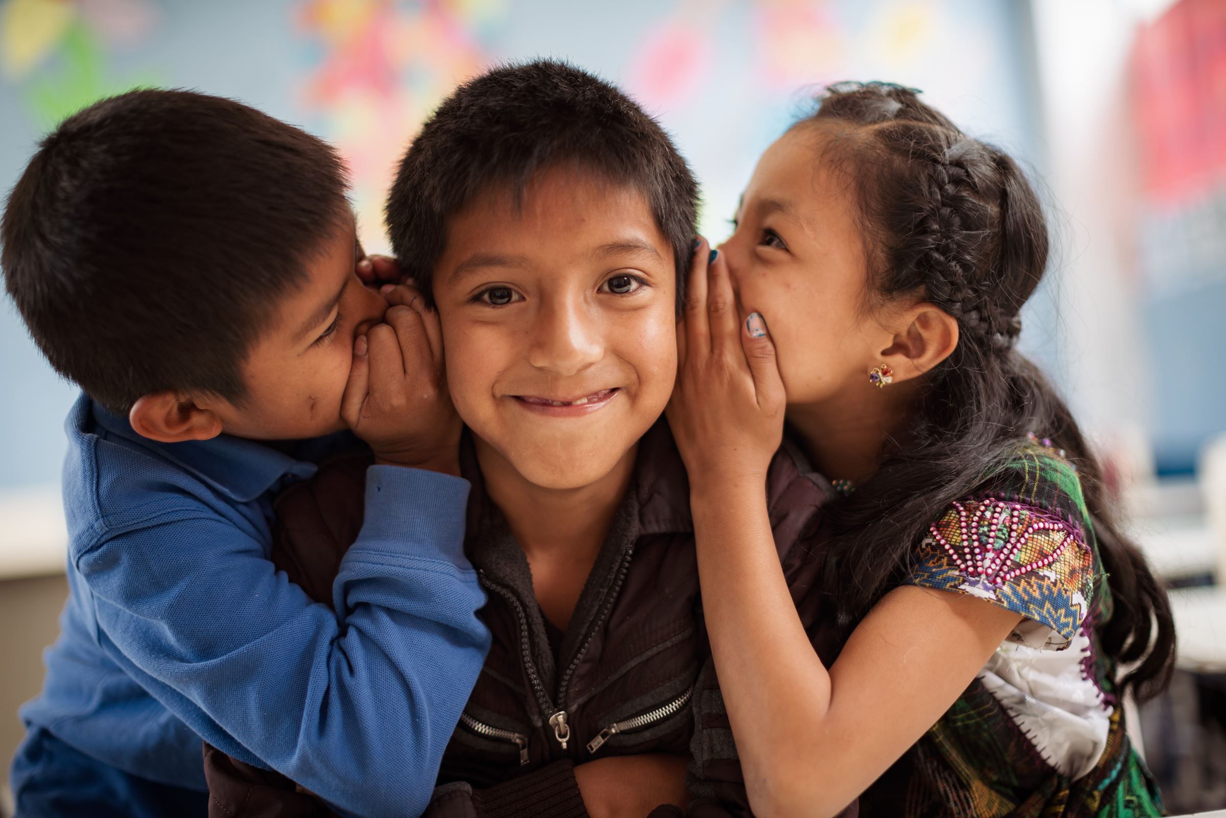 Ein Junge und ein Mädchen flüstern einem Jungen etwas ins Ohr - Guatemala. (Quelle: Jakob Studnar)