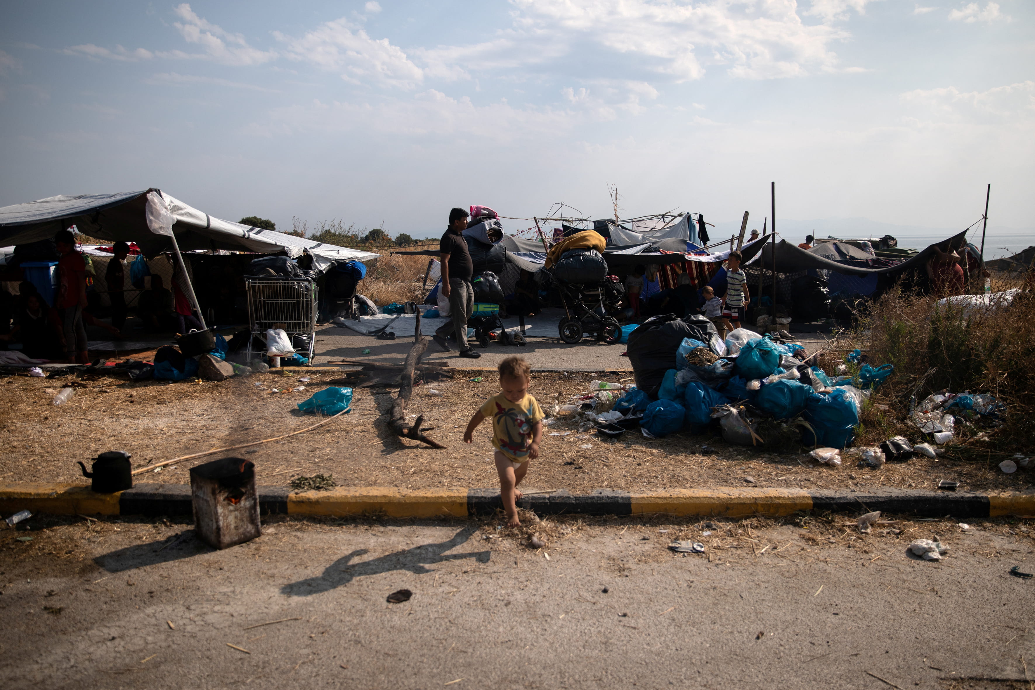 Ein Kleinkind auf Lesbos vor Zelten von Flüchtlingen, die behelfsmäßig am Straßenrand aufgestellt wurden. Daneben Müllberge. (Quelle: Alkis Konstantinidis)