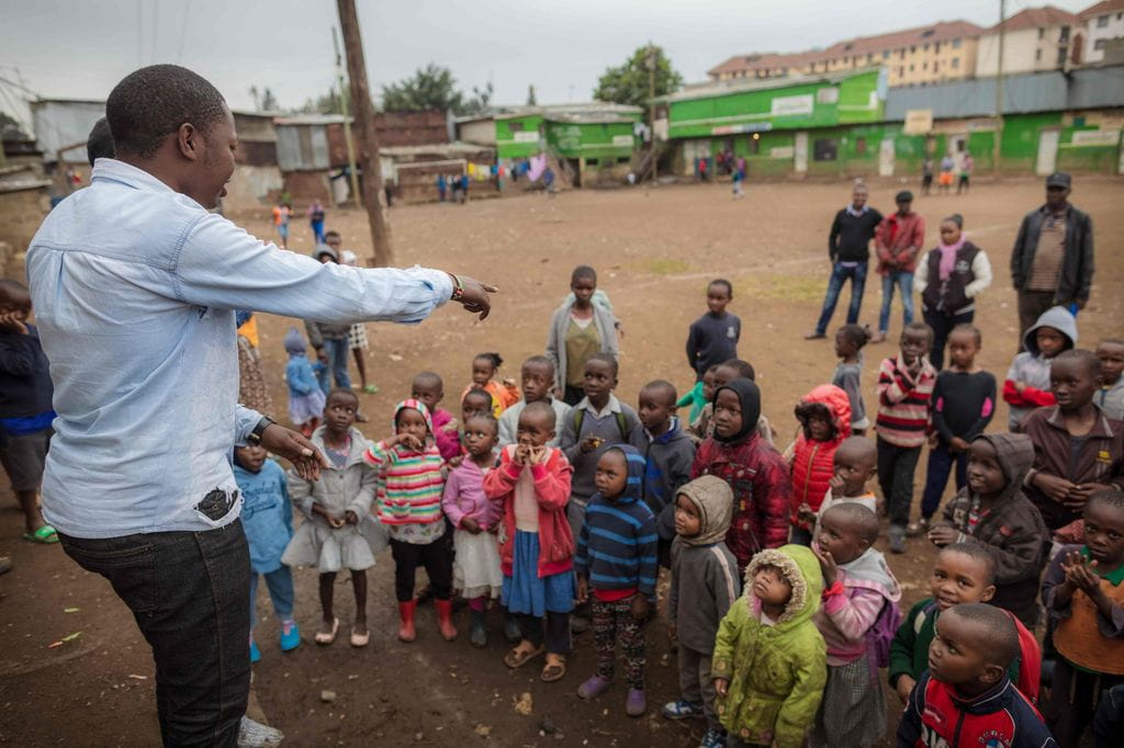 Vorschulkinder bekommen etwas erklärt auf einem Platz, im Hintergrund Wohngebäude (Bildquelle: Lars Heidrich)