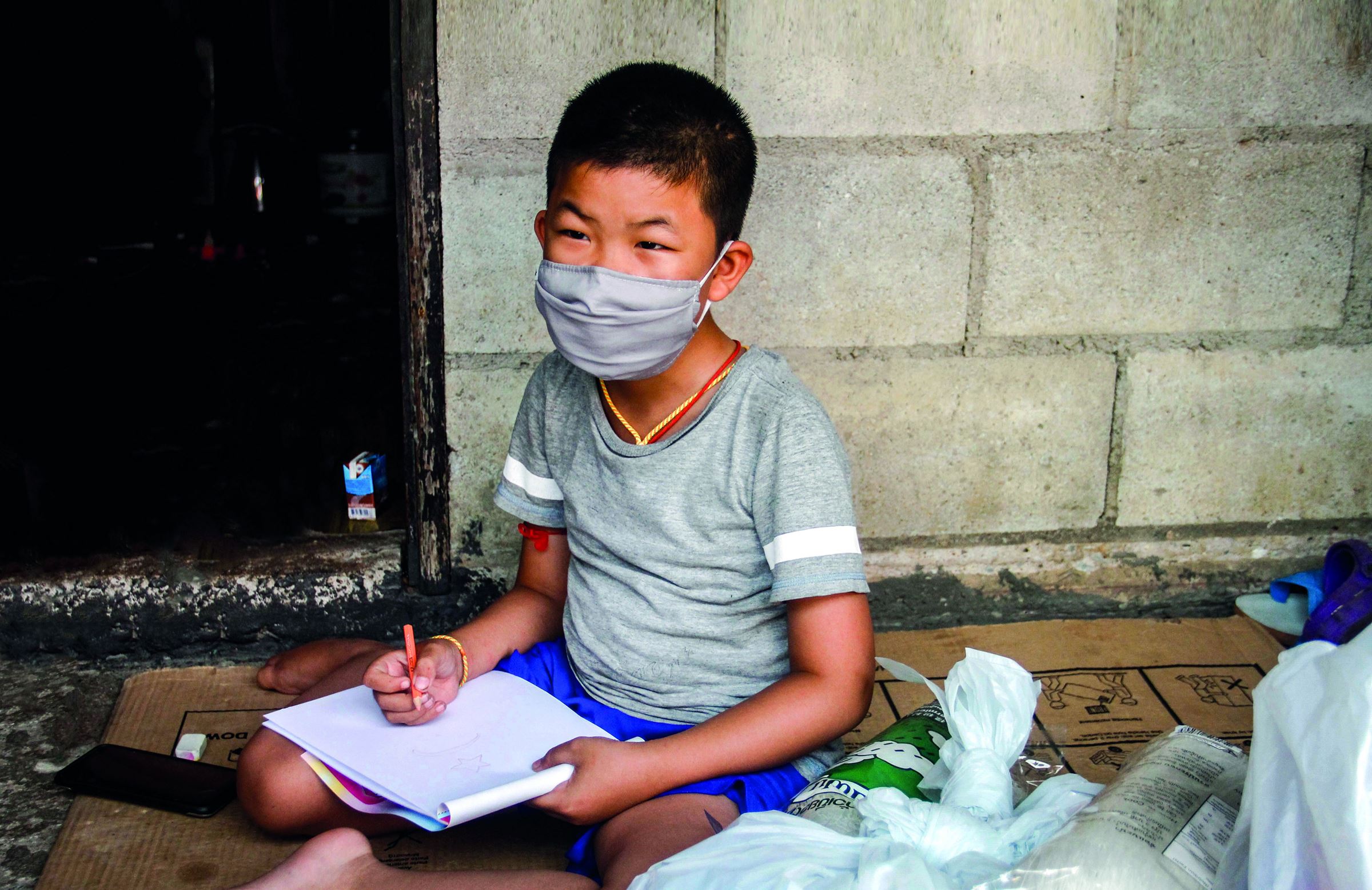 Der thailändische Junge Sai sitzt auf dem Boden und schreibt in einen Block (Quelle: Kindernothilfe-Partner)
