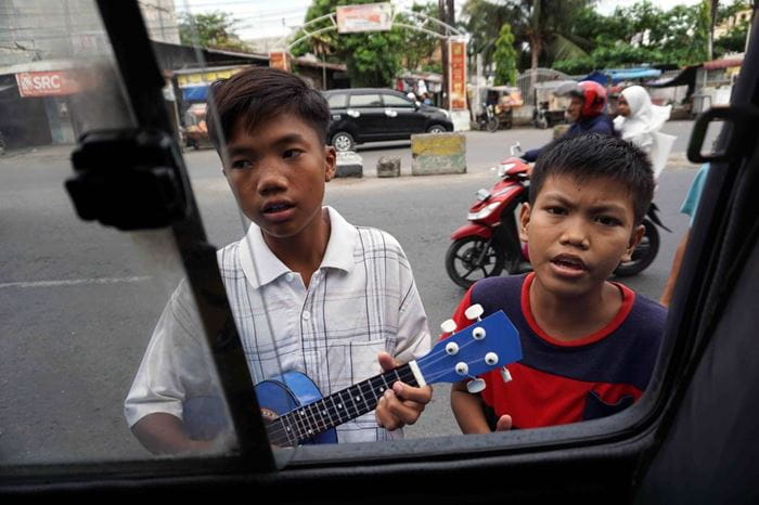 Zwei Jungen singen und spielen Gitarre vor einem geöffneten Autofenster (Quelle: Christiane Dase)
