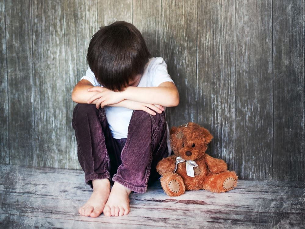 Ein Junge sitzt mit dem Kopf auf den Knien auf dem Boden, neben sich ein Teddy (Quelle: Jakob Studnar) Ein Junge sitzt mit dem Kopf auf den Knien auf dem Boden, neben sich ein Teddy (Quelle: Jakob Studnar)