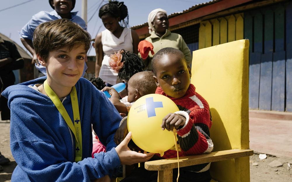 Reportage Kenia: Ein Alltag auf neun Quadratmetern; Foto: Jacob, Kind und Luftballon im Vordergrund, dahinter weitere Kinder und Frauen (Quelle: Dan Zoubek / Kindernothilfe) 