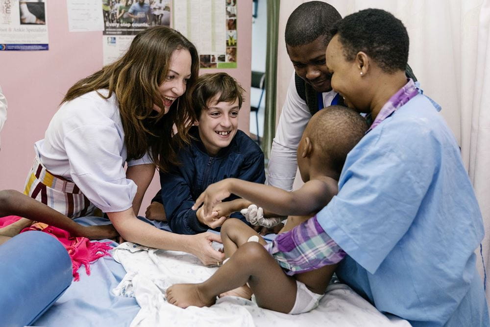 Reportage Kenia: Ein Alltag auf neun Quadratmetern; Foto: Natalia Woerner und Jacob lächeln Kind an, das von Frau mit Kittel gehalten wird (Quelle: Dan Zoubek / Kindernothilfe)  Reportage Kenia: Ein Alltag auf neun Quadratmetern; Foto: Natalia Woerner und Jacob lächeln Kind an, das von Frau mit Kittel gehalten wird (Quelle: Dan Zoubek / Kindernothilfe)