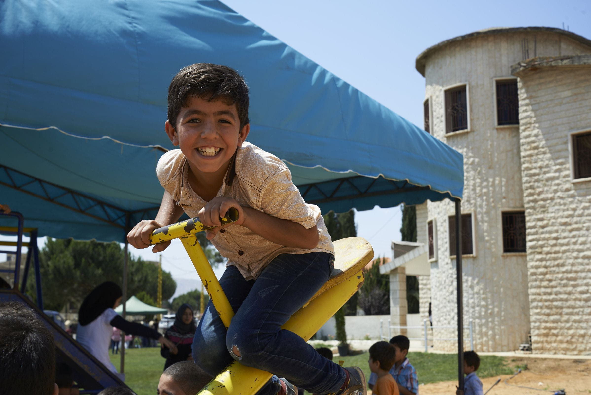 Reportage Libanon; Foto: Kind auf Wippe lacht in die Kamera (Quelle: Ulrich Gernhardt / Kindernothilfe)