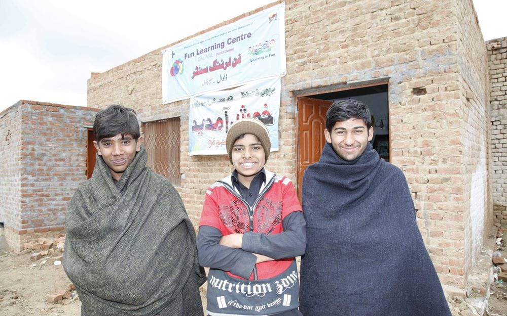 Reportage Pakistan: Das Leben riskieren, um zu überleben; Foto: Drei Kinder stehen vor dem Gebäude des Fun Learning Centers (Quelle: Christian Herrmanny / Kindernothilfe)