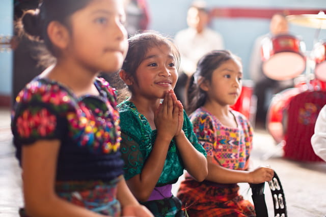 Drei Mädchen sitzen nebeneinander, Mädchen in der Mitte lächelt und faltet die Hände (Quelle: Jakob Studnar)
