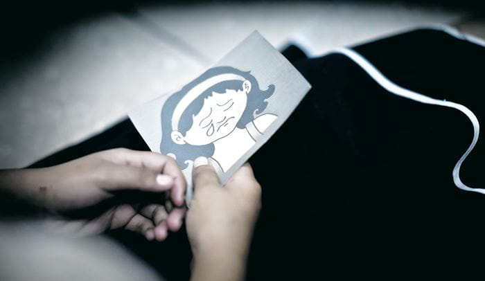 Eine Kinderhand hält eine Pappkarte fest, die ein weinendes Mädchen zeigt. (Quelle: Erika Harzer)