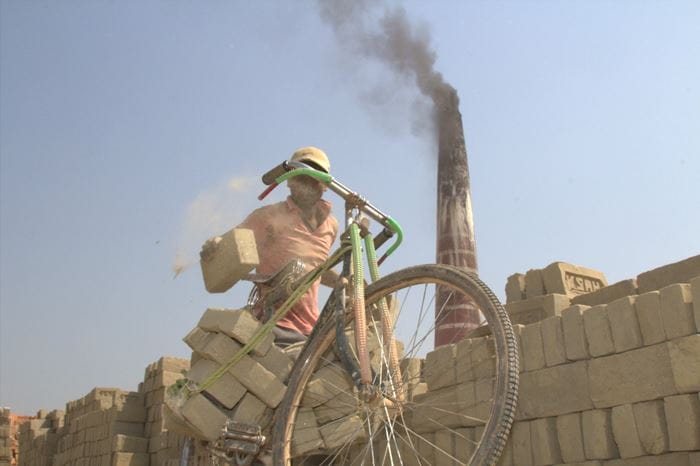 Ein Junge bepackt sein Fahrrad mit frisch gebrannten Ziegeln. Im Hintergrund raucht ein Schlot. (Quelle: Malte Pfau)