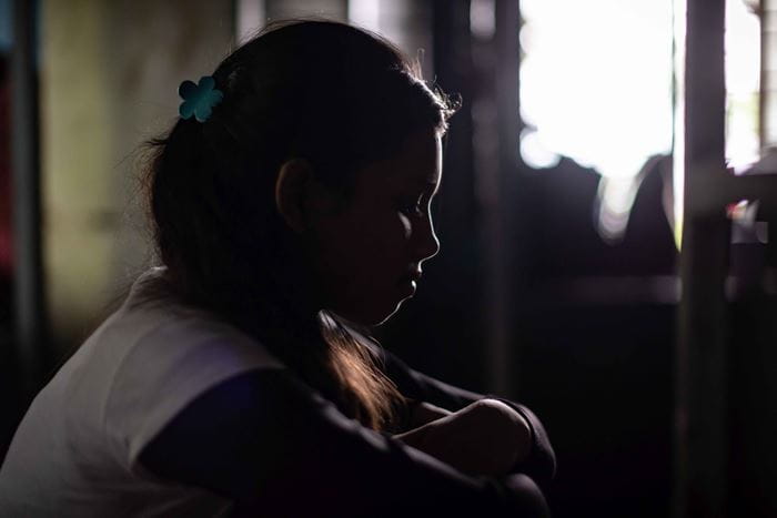 Ein Mädchen im Schatten und im Profil zu sehen, sitzt traurig in einem Raum. (Quelle: Jakob Studnar)