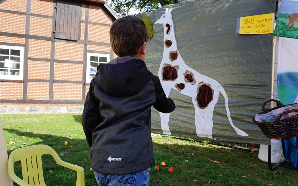Reportage "Ein Dorf in Kindernothilfe-Hand"; Foto: Kind beim Ballwerfen auf gemalte Giraffe (Quelle: Ralf Krämer / Kindernothilfe)