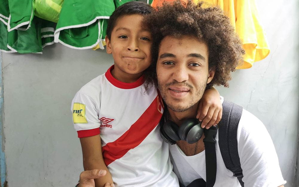 Reportage Peru: "Von Selbstvertrauen und Kinderrechten"; Foto: Kind und Dillan White sitzen nebeneinander und blicken in die Kamera (Quelle: Lorenz Töpperwien / Kindernothilfe)