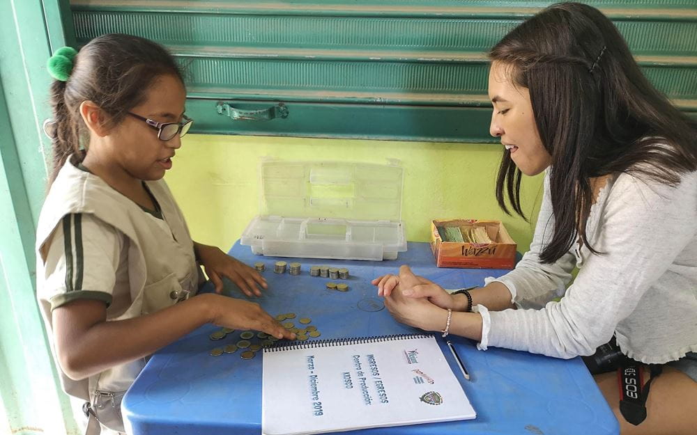 Reportage Peru: "Von Selbstvertrauen und Kinderrechten"; Foto: Kind und Shanti Tan sitzen sich an einem Tisch gegenüber (Quelle: Lorenz Töpperwien / Kindernothilfe)