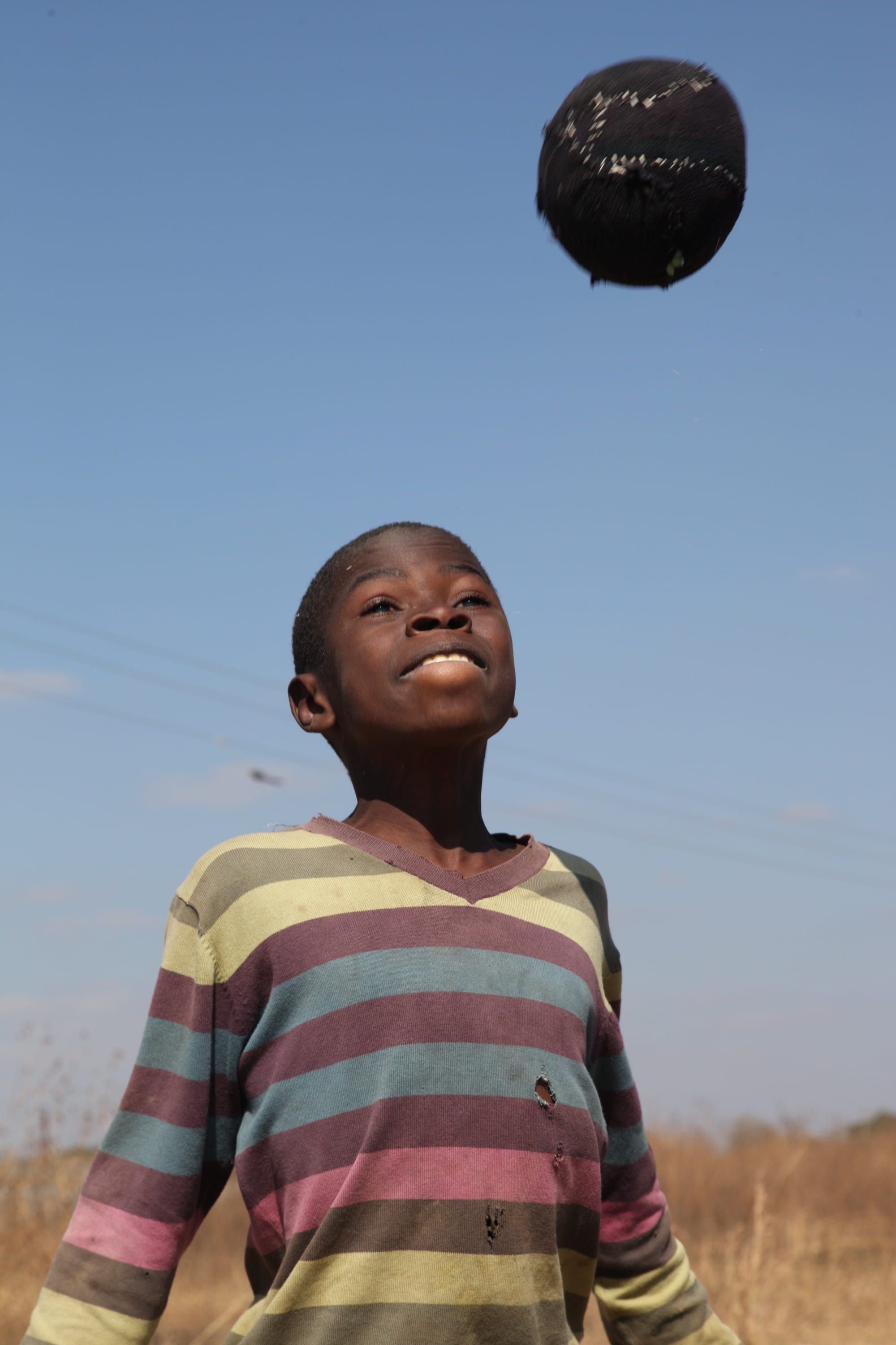 Ein Kind spielt mit einem Fußball aus Müll.