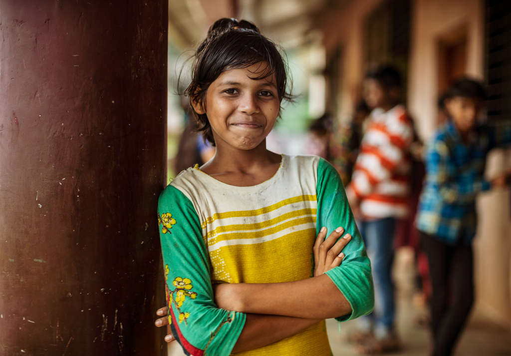 Ein Mädchen aus Indien steht an eine Säule gelehnt und lächelt. (Quelle: Jakob Studnar)