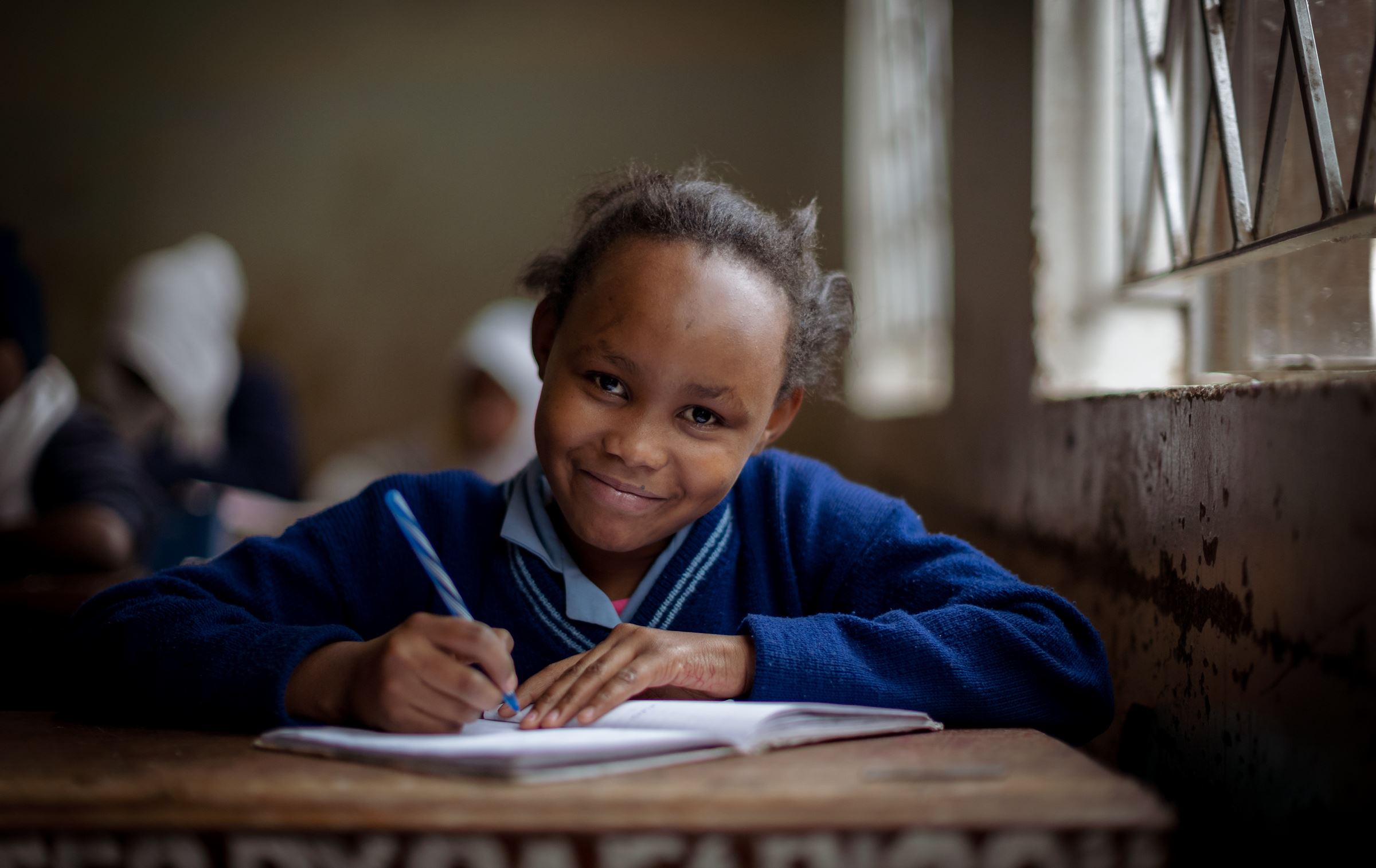 Ein Mädchen lächelt, sie hält einen Stift in der Hand. (Quelle: Lars Heidrich)