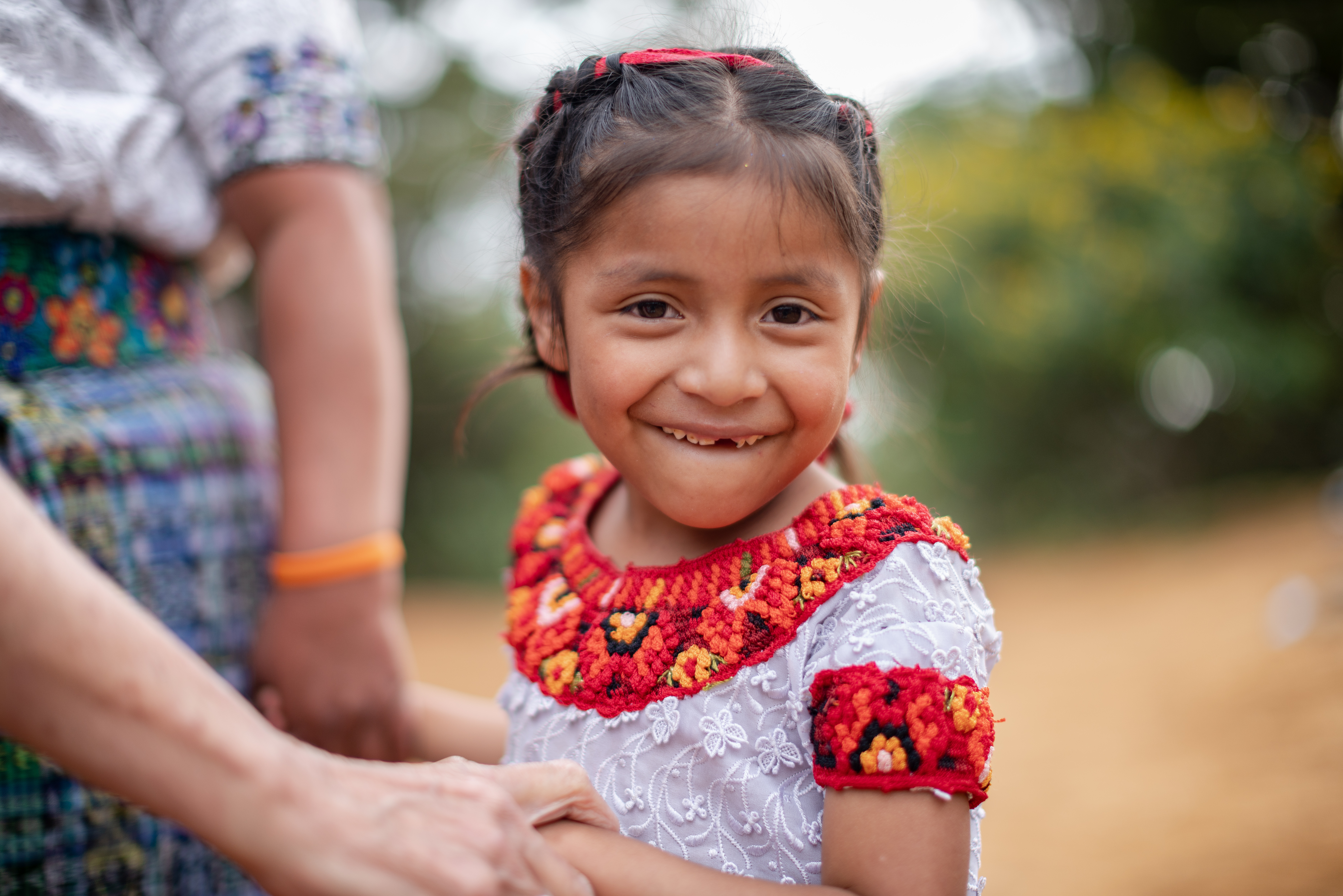 Ein kleines Mädchen mit Zahnlücke lächelt, sie steht neben einer Frau im Hintergrund. (Bildquelle: Jakob Studnar)